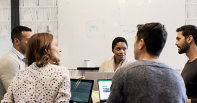 Cinque persone che collaborano sui portatili a un tavolo