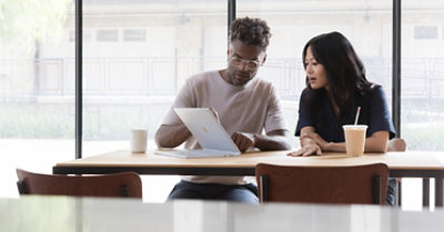 Two people working together using a Surface Pro in studio mode. One of them is drinking a smoothie.