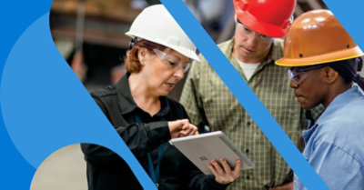 Tres trabajadores de primera línea con cascos en un sitio de trabajo mirando una tableta.