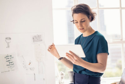 Una persona se encuentra en una oficina iluminada, sosteniendo y mirando una tableta. 