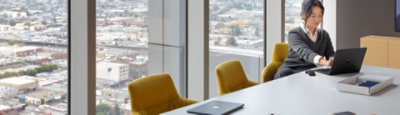 Person using a laptop while seated at a large conference room table in an office building high above a city