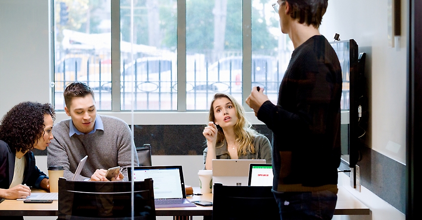 Four people meeting in a conference room with devices open