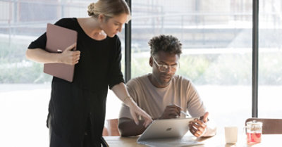 Personne assise et tenant un appareil Surface. Une autre personne se penche au-dessus de son épaule et désigne quelque chose sur l’écran
