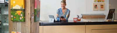 A person standing at a desk next to a tablet device and using a mobile device.