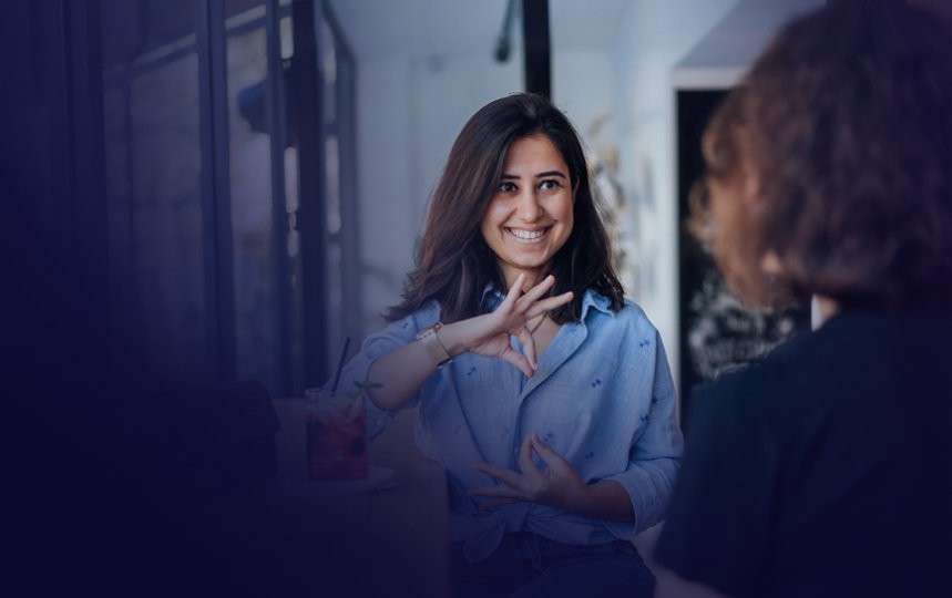 A woman in a café uses sign language to communicate with another person at the counter.