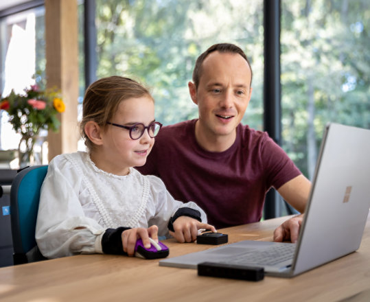 A young girl uses a Surface Laptop with accessibility aides from the Microsoft Adaptive Accessories collection.