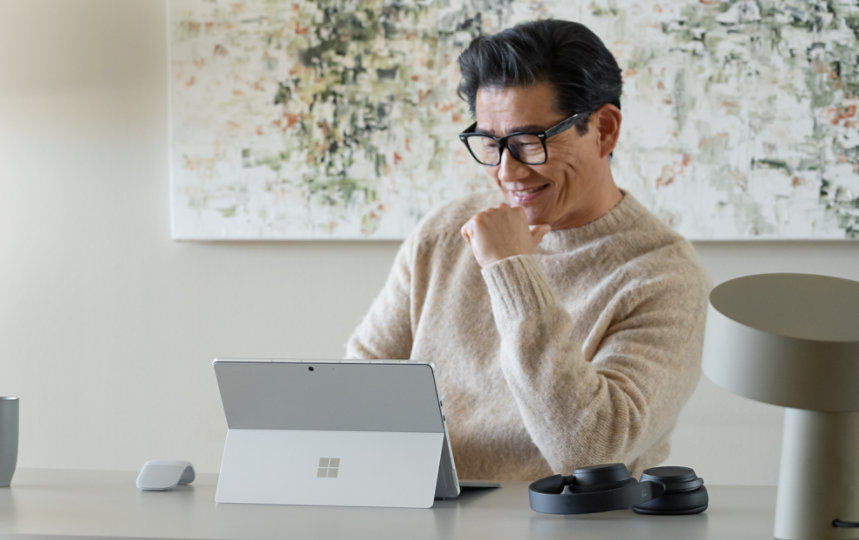 ホームオフィスのデスクの前に座り、Surface Pro 9とSurfaceアクセサリを使って仕事をする男性。