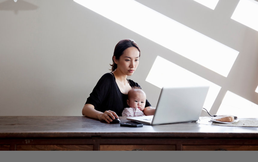 赤ちゃんを抱きながらノートパソコンを使って自宅で働く女性。 