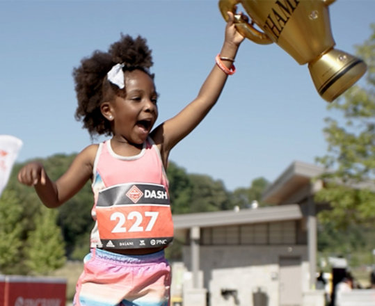 A young runner holds up a trophy triumphantly.