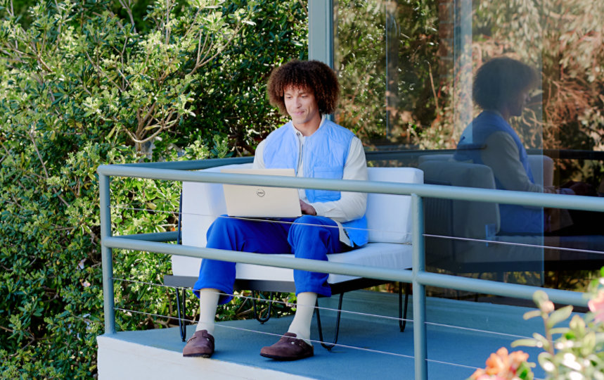 Um homem se concentra intensamente em seu notebook e está sentado em uma sacada.