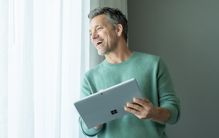 A man standing in a hotel room holding a Surface Pro 9 with 5G in Platinum.