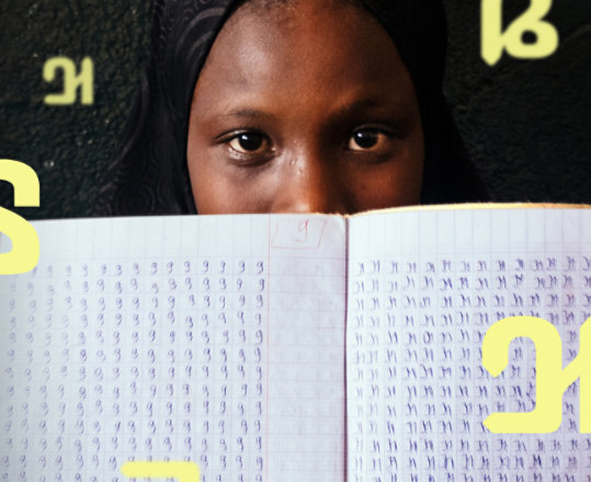 A woman holding a notebook filled with ADLaM script.