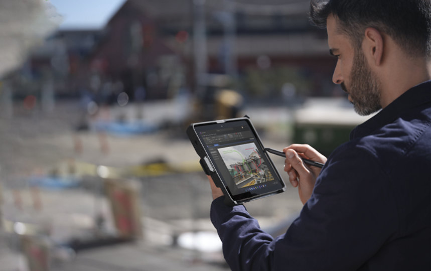 Un homme adulte sur le terrain tenant une Surface Go 3 dans un étui renforcé « Conçu pour Surface » en mode tablette, tout en écrivant sur une Microsoft OneNote avec un stylet pour Surface.