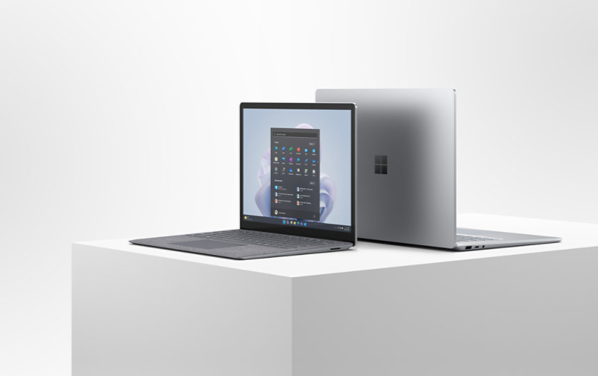 A 13.5” and a 15” Surface Laptop 5 for Business sit open and back to back on a platform.