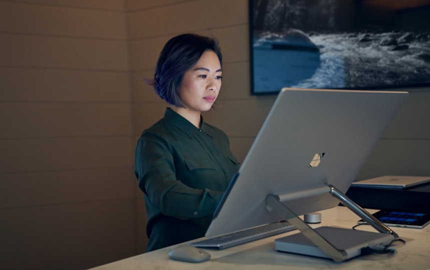 Side profile of a woman wearing a dark shirt in a dim office working on a Microsoft Surface Studio.