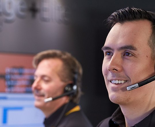 Two people wearing headsets and working at their desks