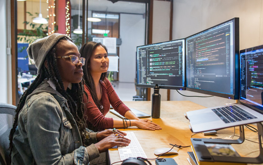 Kolleginnen und Kollegen verwenden Visual Studio auf mehreren Desktop-Monitoren bei der Arbeit.