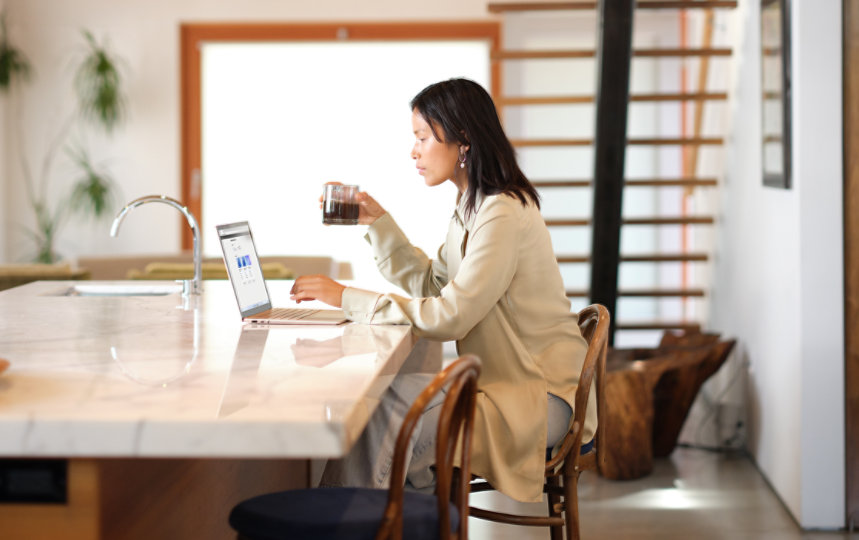 キッチンでコーヒーを飲みながら Windows 11 コンピューターを使用している女性