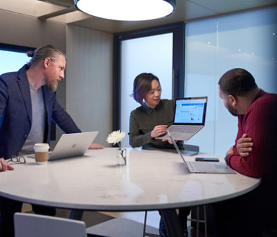 Three people are discussing at their desk.