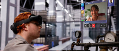 A person wearing AR glasses in an industrial setting interacts with a virtual screen showing a video call with a smiling person. 