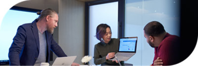 Una persona sostiene una computadora portátil para mostrar la información que allí aparece a dos compañeros de trabajo.