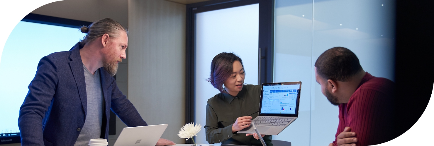 En person, der holder en bærbar computer og viser dens skærm til to kollegaer.