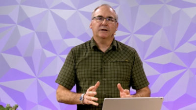 一个人正在讲话，他面前放着一台笔记本电脑。