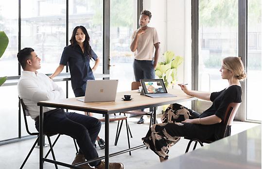 Toplantı yapan dört kişinin ve küçük konferans masasında açık duran iki dizüstü bilgisayarın fotoğrafı.