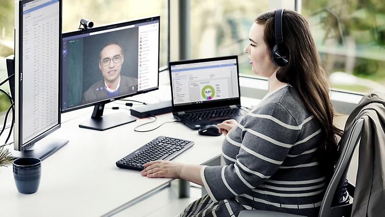 A person wearing over-the-ear headphones working at their desk with multiple screens and participating in a Teams call.