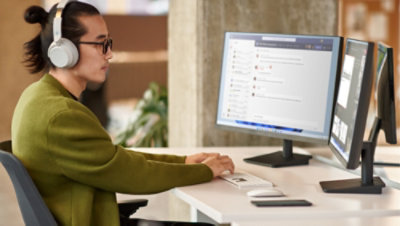 Una persona indossa cuffie on ear mentre lavora a una scrivania con due monitor e una tastiera Bluetooth.