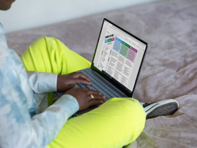 A person sitting on the floor using a laptop to assess which Microsoft tool would be best for them.