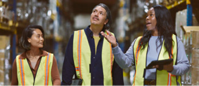 A group of people wearing safety vests walking through a warehouse.