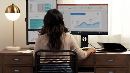 Uma pessoa sentada num escritório em casa a olhar para dados em dois monitores de computador.