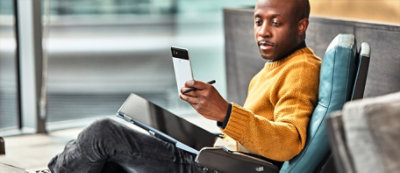 Una persona seduta sul divano ha uno smartphone in una mano e uno stilo che usa sul tablet nell'altra.