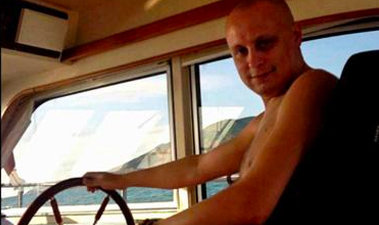 A shirtless person looks toward the camera while appearing to navigate a vessel in a body of water that is barely visible in the background