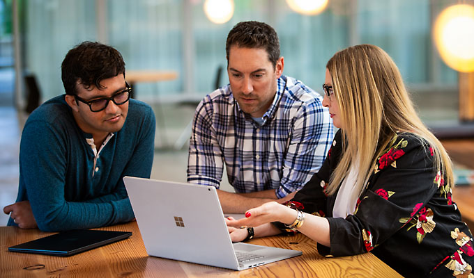 Three people seated around a table looking at a laptop