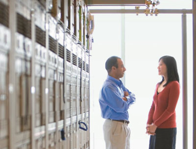 廊下で、サーバーが並んだ壁の前に立って話している 2 人の人。