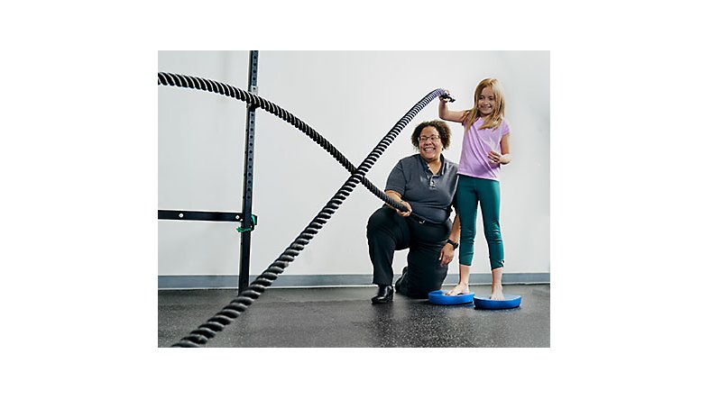 A healthcare provider helping a child use physical therapy ropes