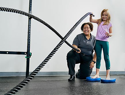 A healthcare provider helping a child use physical therapy ropes