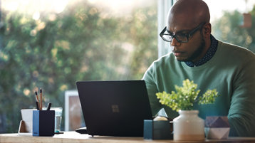 A person wearing glasses seated at a desk using a laptop.