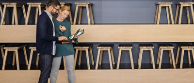 שני אנשים עומדים ומביטים יחד במחשב נישא מול קיר עם שורות רבות של שרפרפים בערימות.