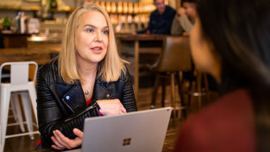 Δύο άτομα που συνομιλούν σε μια καφετέρια, πάνω από έναν φορητό υπολογιστή.