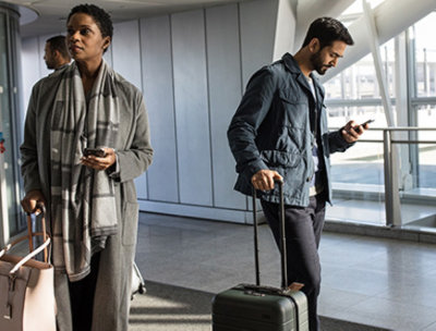 Two people with luggage waiting at an airport gate and using mobile devices
