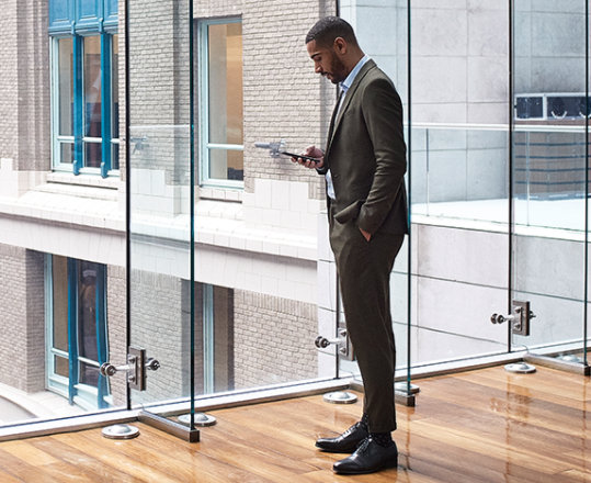 A person standing in an enclosed walkway between two buildings. They are looking at a mobile device.