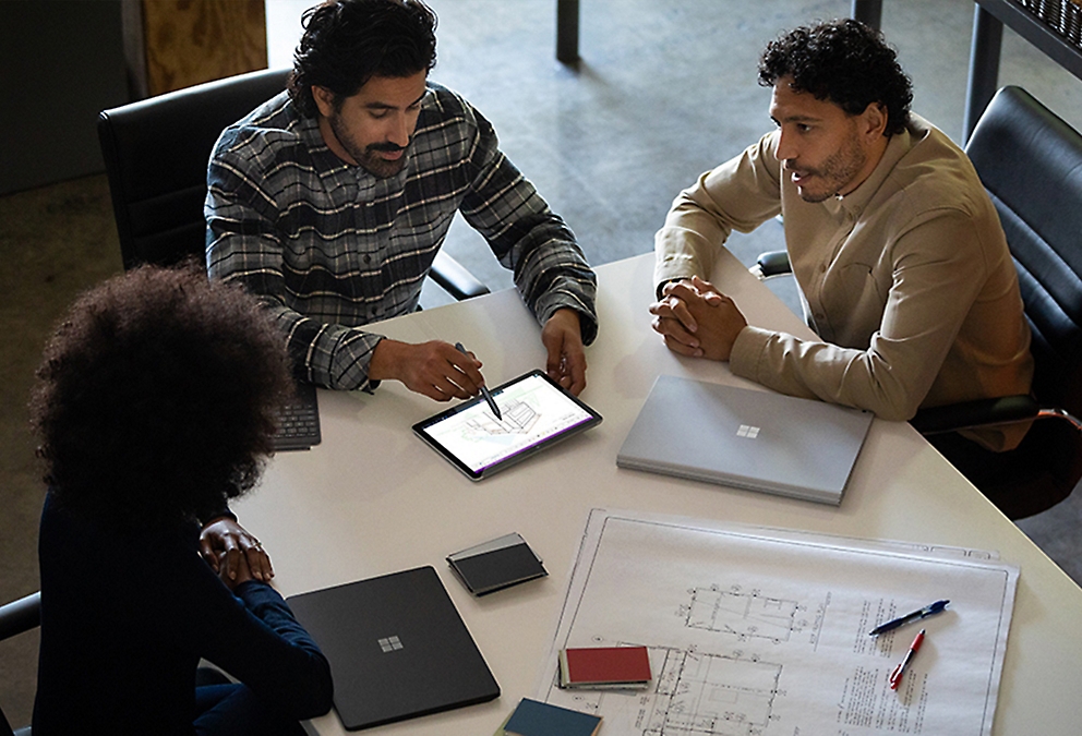 Three people seated around a table looking at an architectural design on a tablet