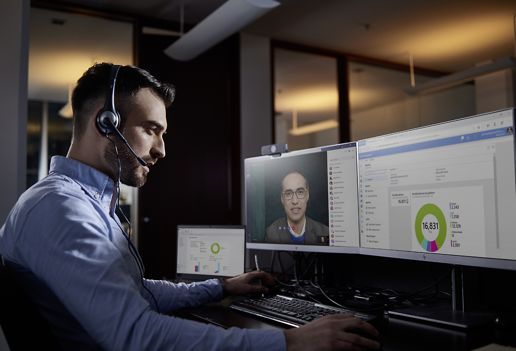 Een persoon in een telefonische vergadering die een headset draagt en een presentatie deelt op twee beeldschermen.