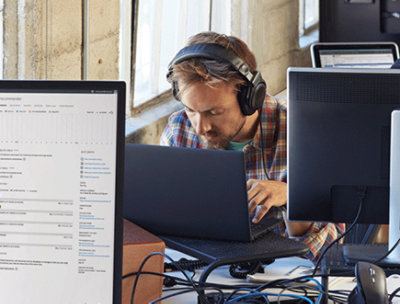A person wearing headphones looking down and using a laptop.