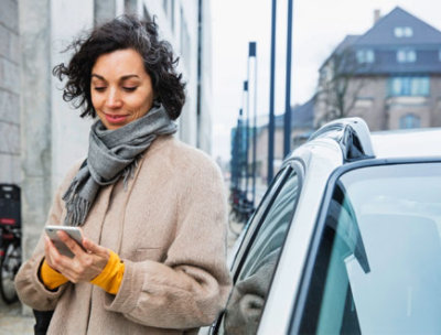 Eine Person im Freien, die sich an ein Auto lehnt und ein Mobiltelefon benutzt