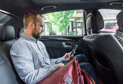 Photograph of a person in the backseat of a car looking at a mobile device
