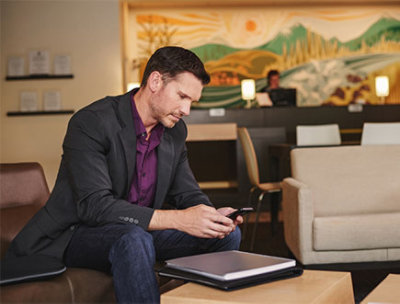 Ein Kunde, der in einem Wartebereich auf einer Bank sitzt und ein Mobiltelefon nutzt